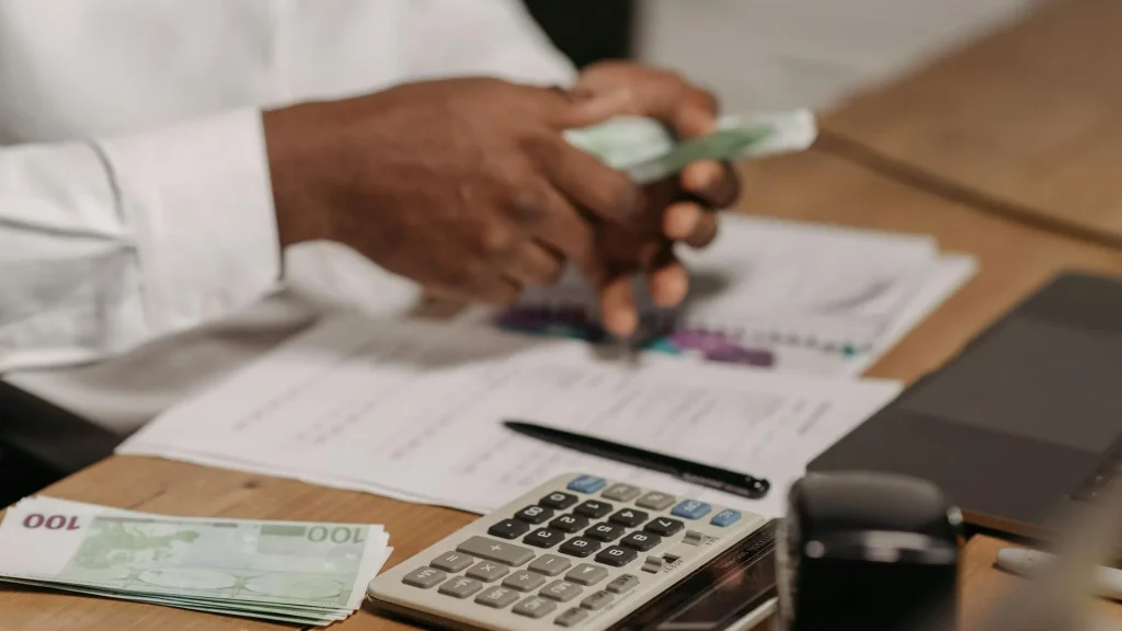 Mãos a contar notas de euro em secretária com calculadora e documentos